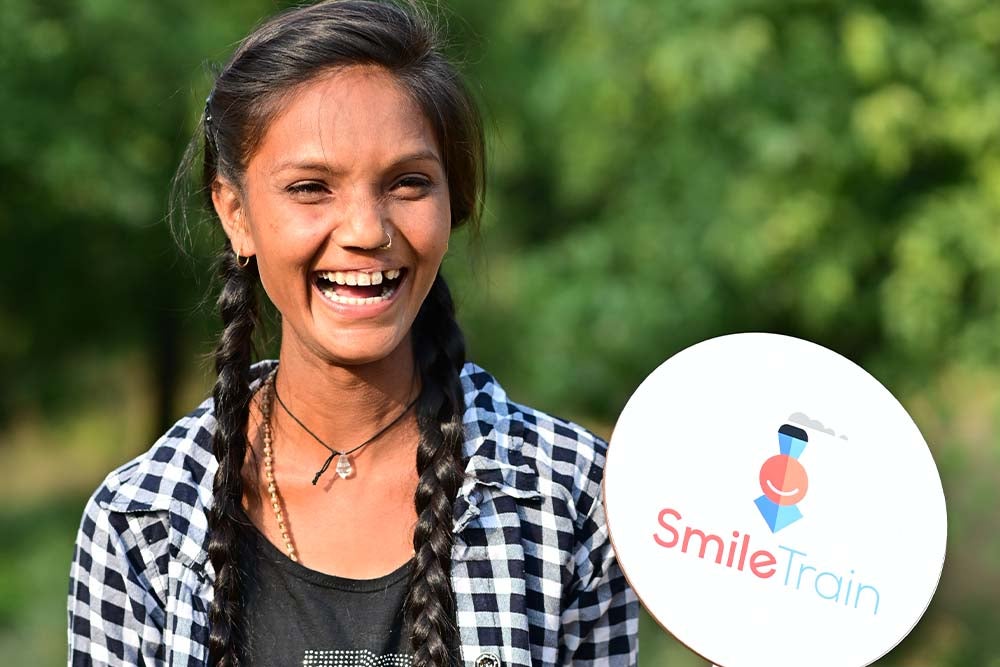Pinki souriant en tenant une affiche Smile Train