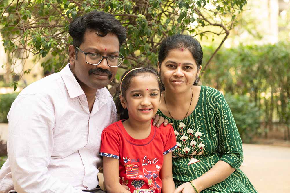 Durva sits smiling with her father, Nilesh, and mother, Poonam