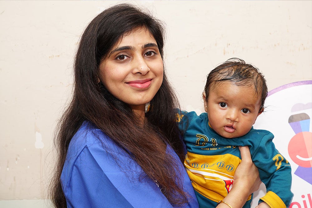 Payal smiling, holding a baby after cleft surgery