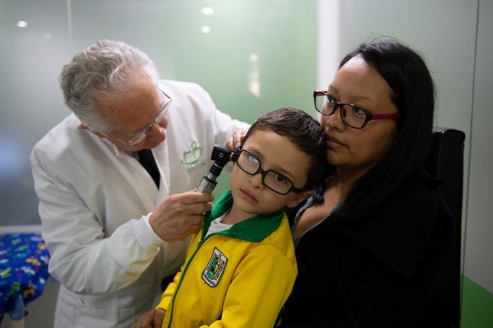 Assis sur les genoux de sa mère, un enfant avec une fente reçoit les soins d’un audiologiste qui vérifie son audition.
