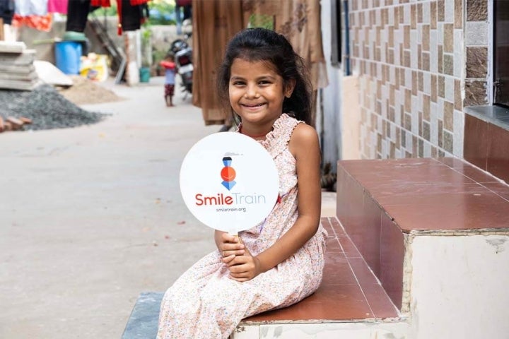 Un patient de Smile Train sourit et tient une affiche Smile Train après sa chirurgie de la fente